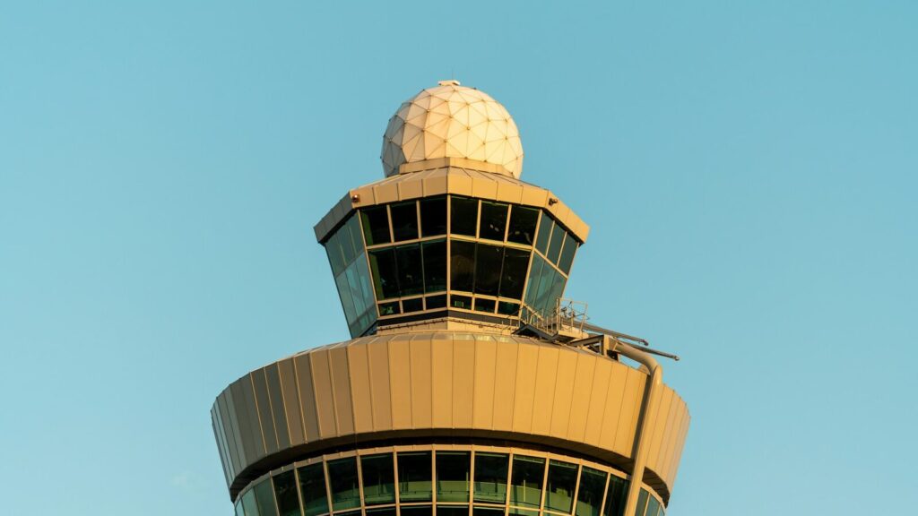 Verkeerstoren van Schiphol in warm licht tegen een heldere blauwe lucht